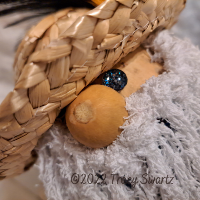 Close up of a gnome face made from a hard shell gourd with a gourd nose, straw hat, white yarn beard and one glittery eye peeking