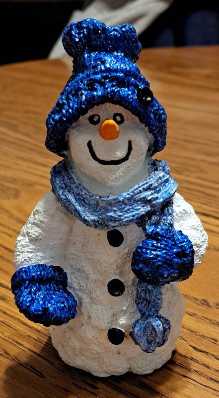 Snowperson wearing a blue hat with black button, light blue scarf and blue mittens